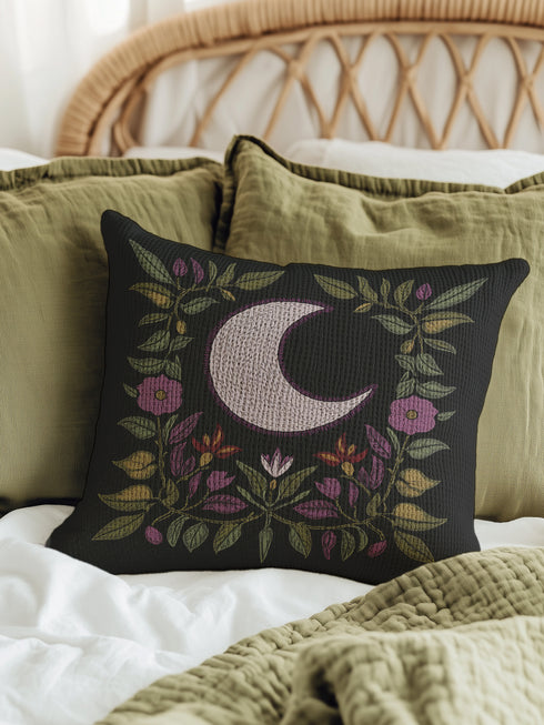 Black woven throw pillow with an embroidered crescent moon and floral pattern in soft ivory, green, purple, and gold, featuring a textured finish.